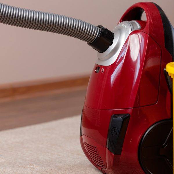 Red vacuum cleaner and plastic bucket with liquid detergents on beige carpet. Housekeeping concept
