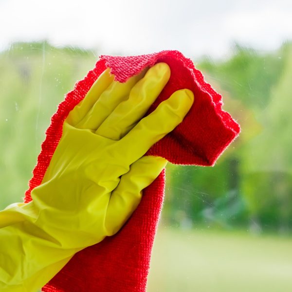 Window washing and home cleaning. Housekeeper in yellow gloves washes and wipes dirty glass.