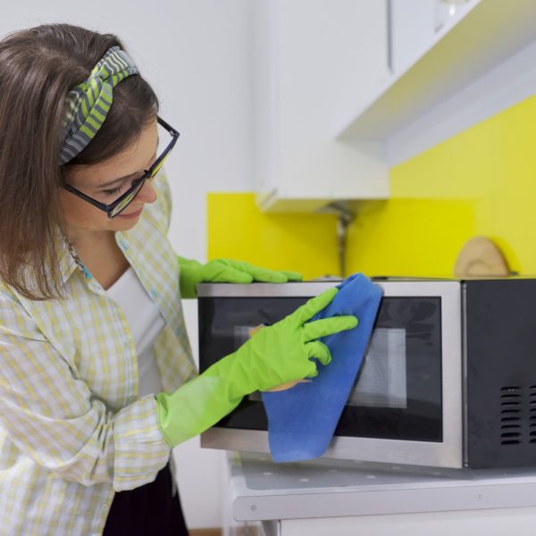 Woman in protective rubber gloves with rag cleaning microwave at home in the kitchen